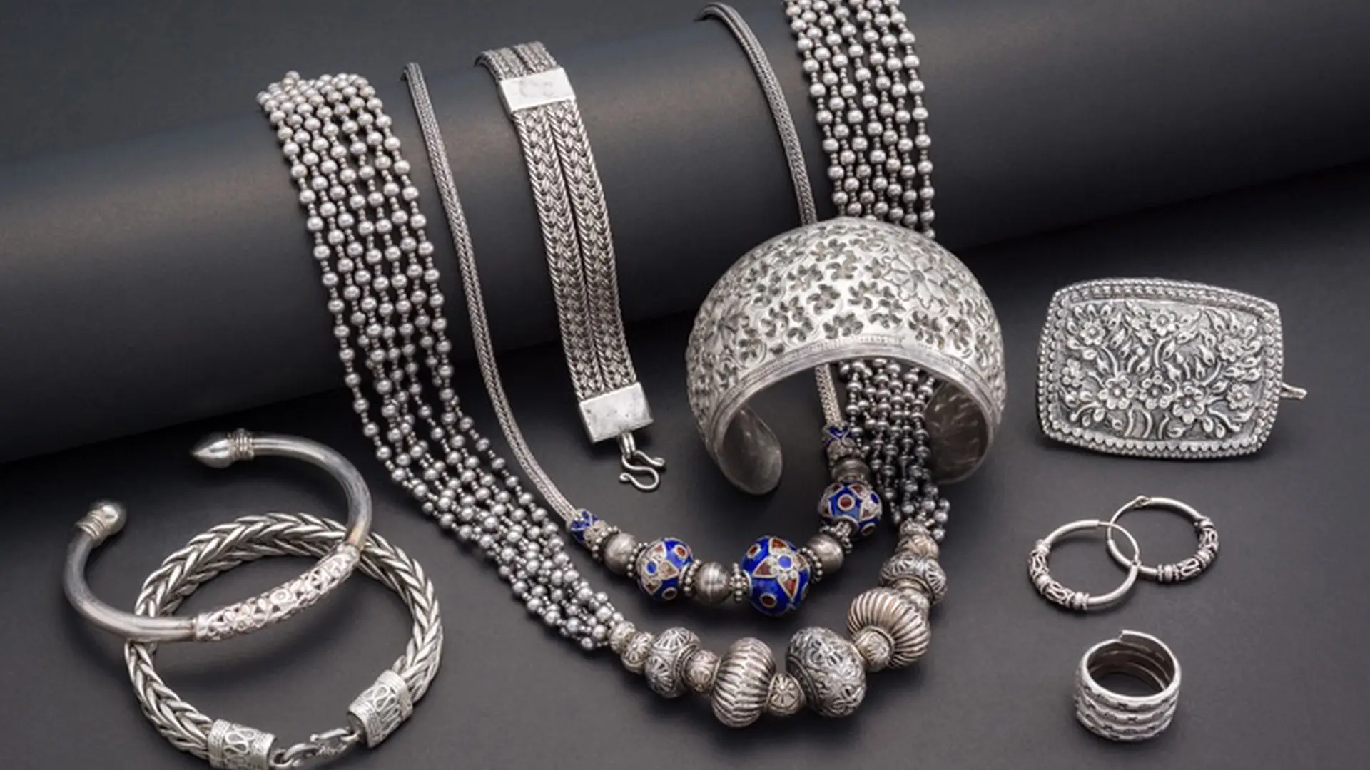 Ornate sterling silver necklaces, filigree cuff and bangles on a dark surface.